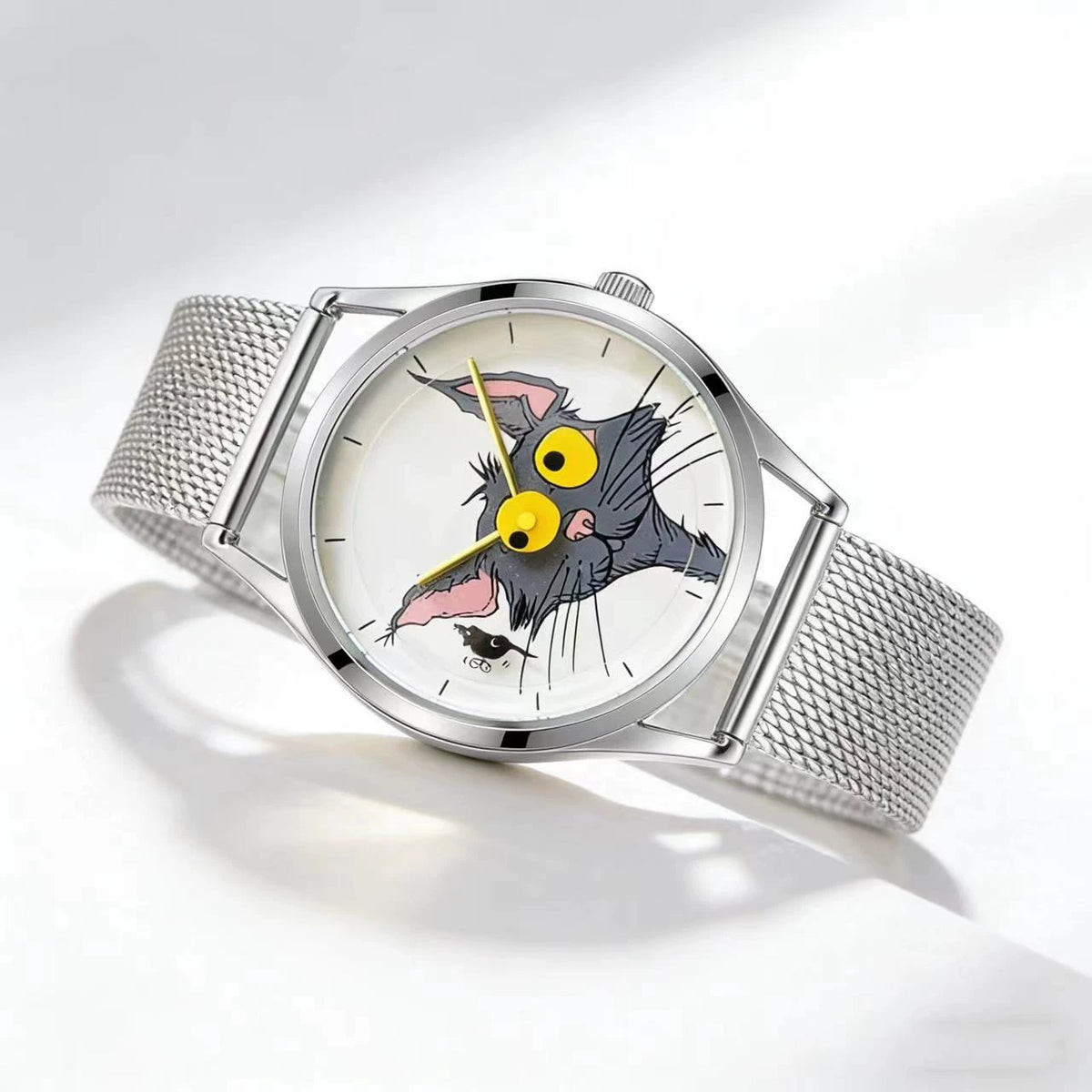 Angled view of Chase Me, Kitty! watch with illustrated cat-and-mouse dial, yellow hands and silver mesh strap on a white surface