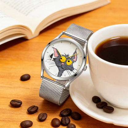 Chase Me, Kitty! cat dial watch with silver mesh strap beside a coffee cup, coffee beans and an open book on a wooden table