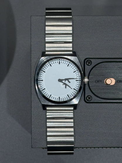 Top view of CHOOSZ Arcade Loadout watch on a black speaker, showing white dial, gun-shaped hands and silver steel bracelet