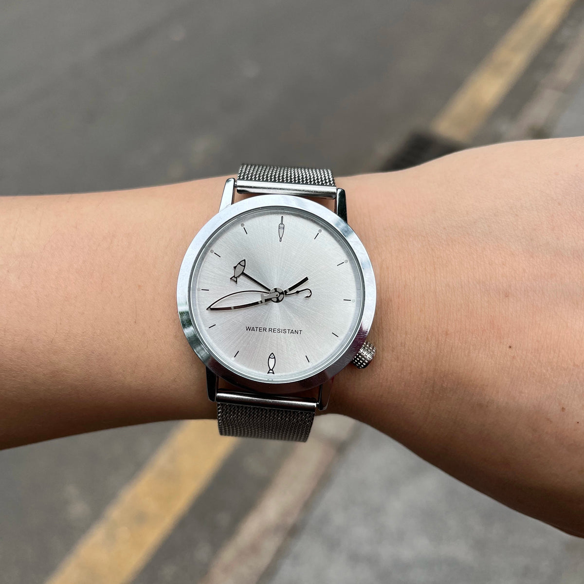 CHOOSZ Lucky Cast watch worn outdoors, showing its silver fishing-themed dial and stainless steel mesh strap