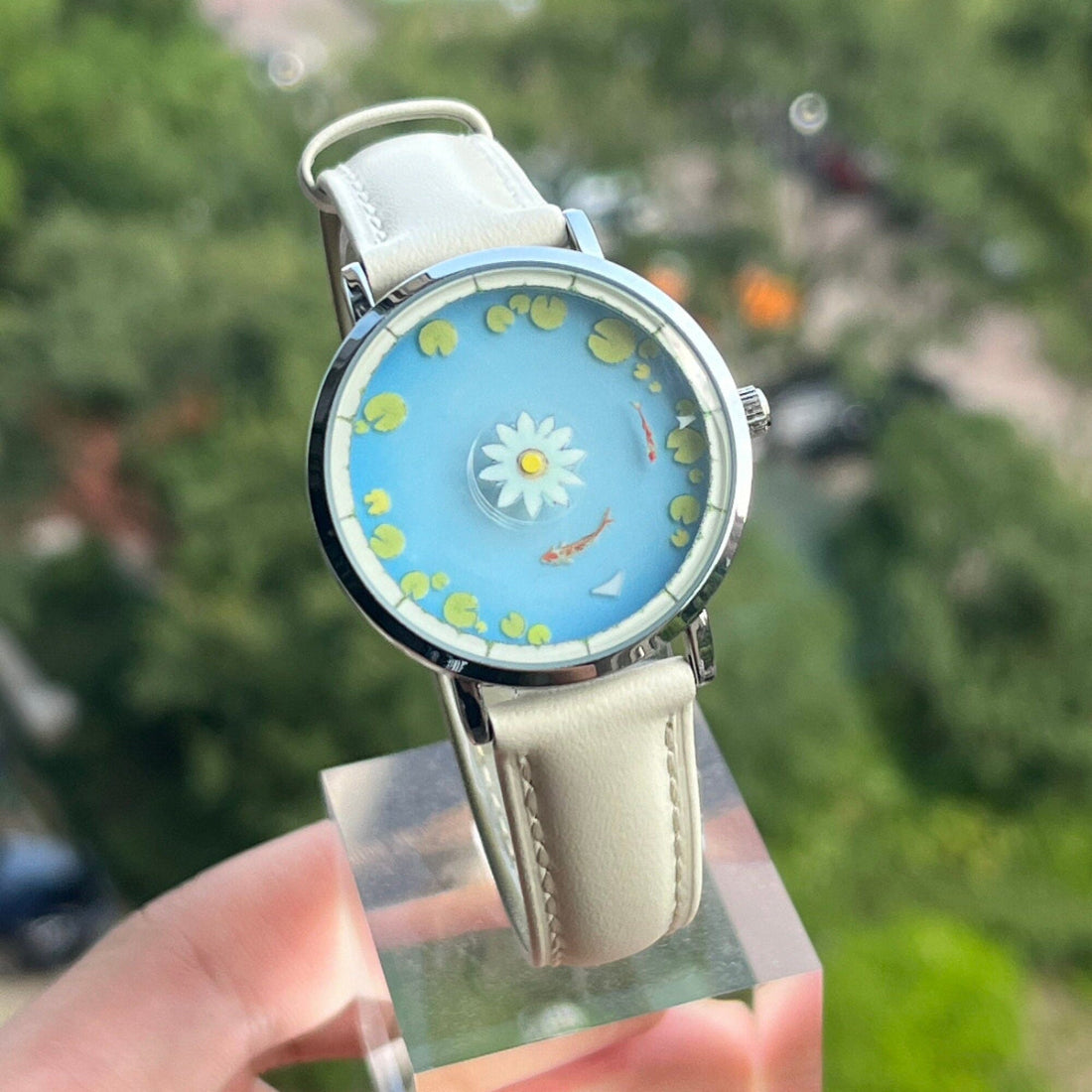 Aqua Animism koi e orologio loto tenuto all'aperto contro il fogliame verde