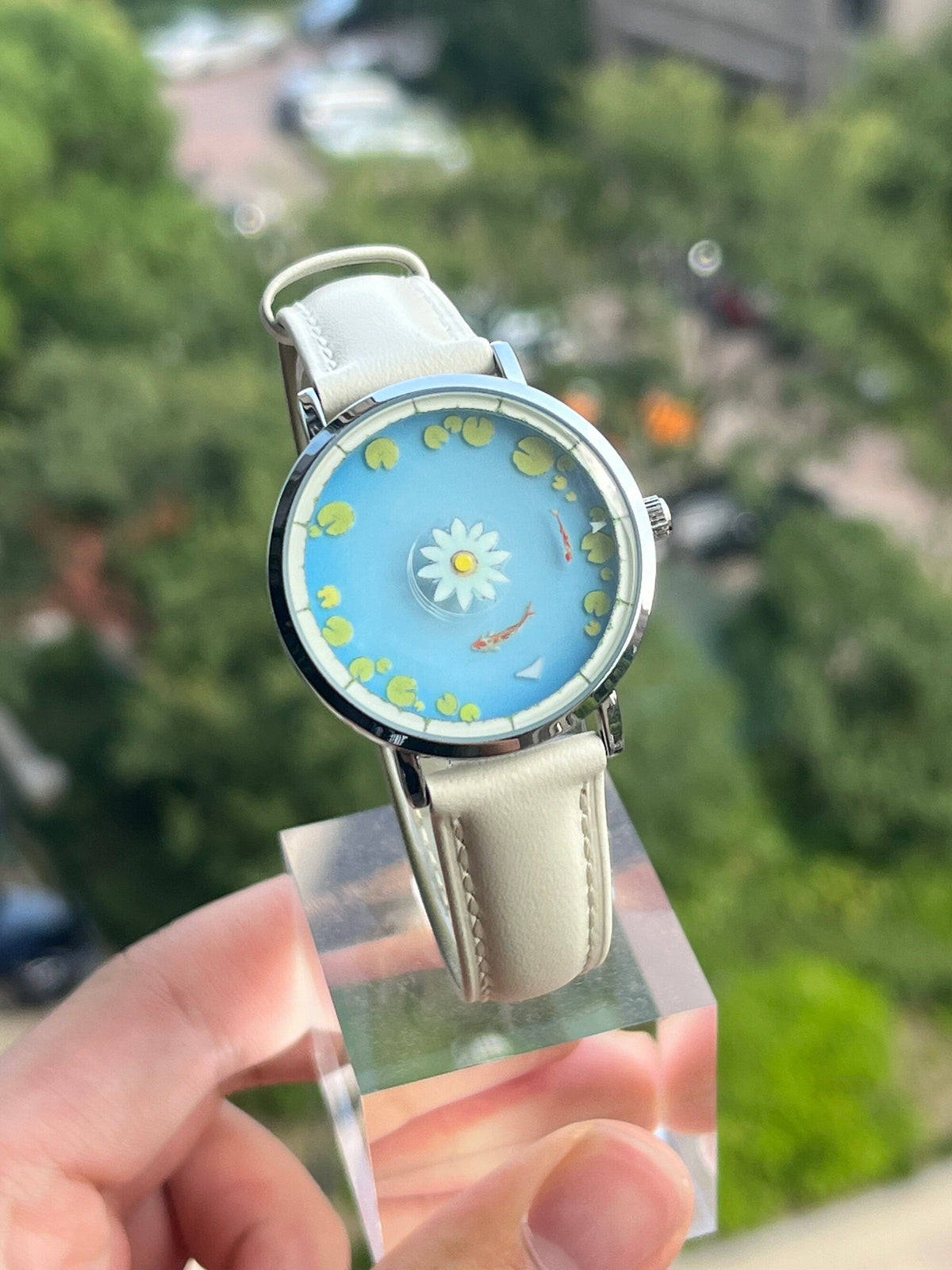 Aqua Animism koi and lotus watch held outdoors against green foliage