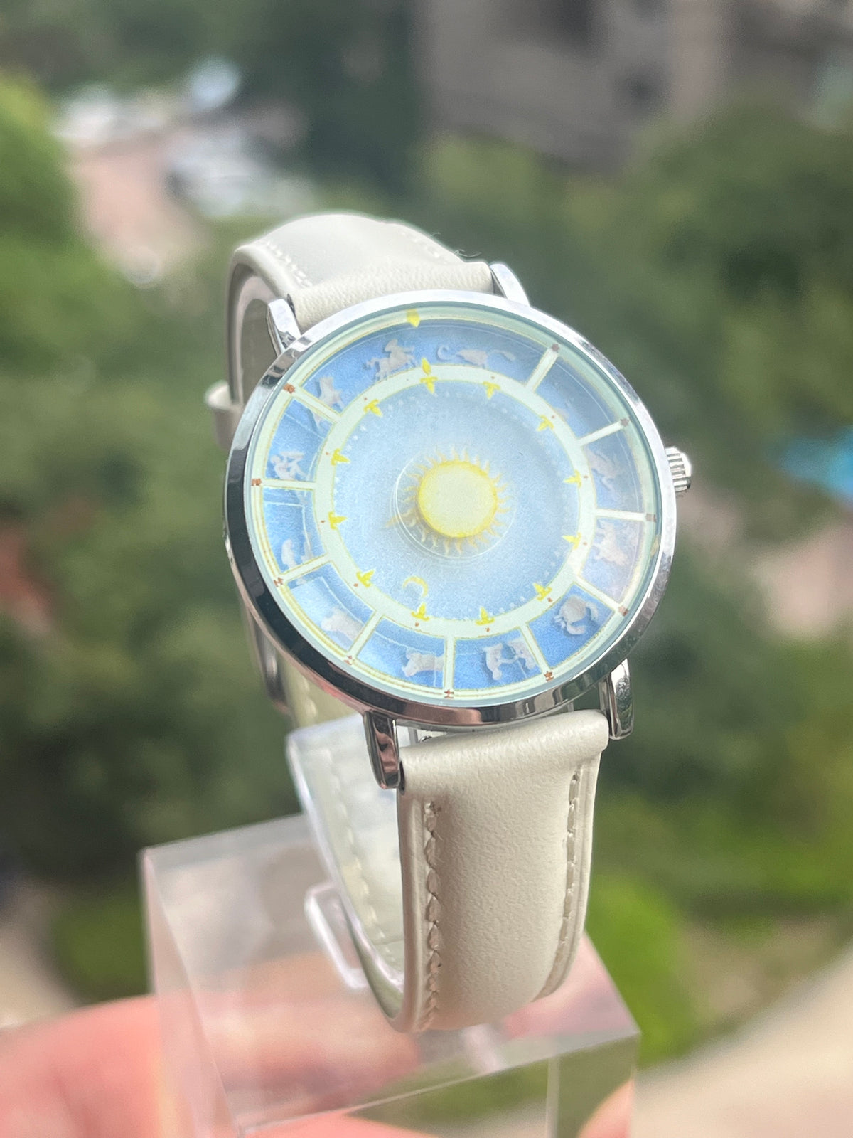 Astral Mythos zodiac watch held outdoors against green foliage