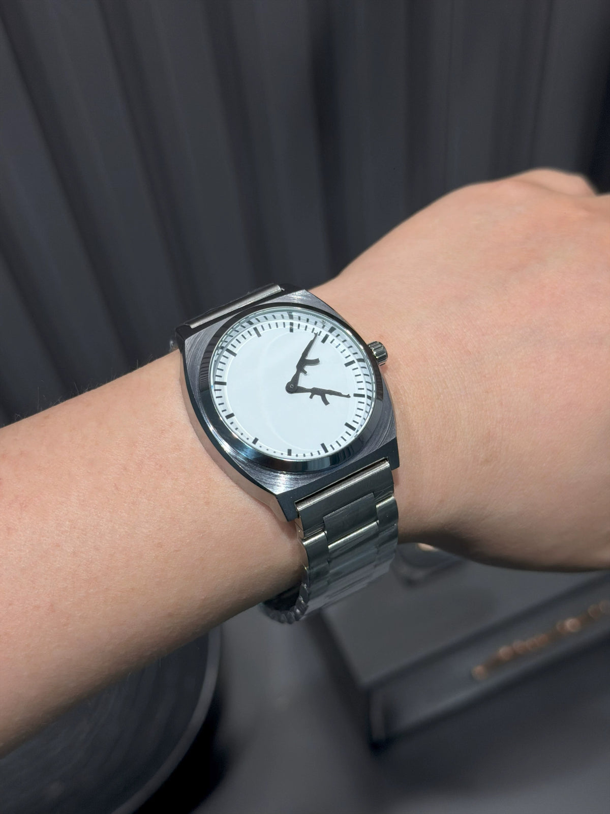 CHOOSZ Arcade Loadout watch worn on the wrist, with white dial, black gun-shaped hands and silver steel bracelet