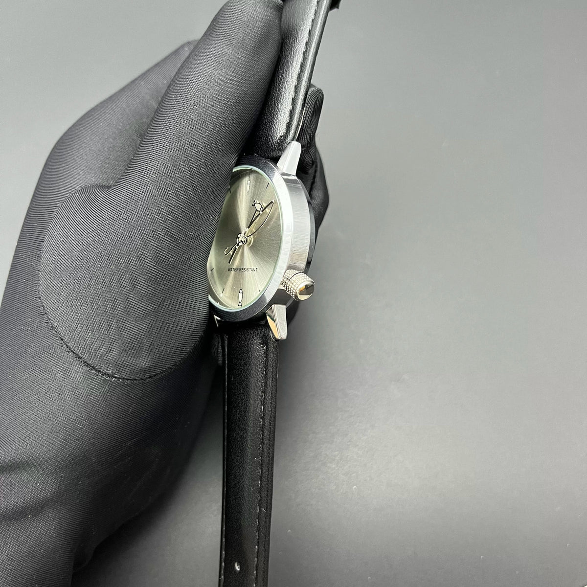 Side-angle close-up of CHOOSZ Lucky Cast watch held in a glove, showing silver case, textured crown and black leather strap