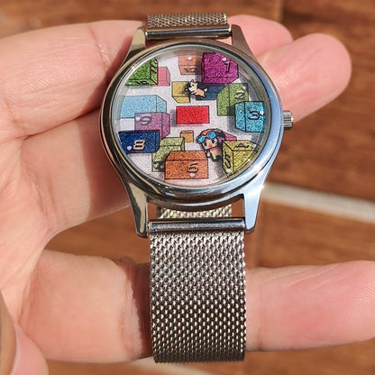 CHOOSZ Weightless Hours watch held in a hand, showing its colorful numbered-block dial and silver mesh bracelet