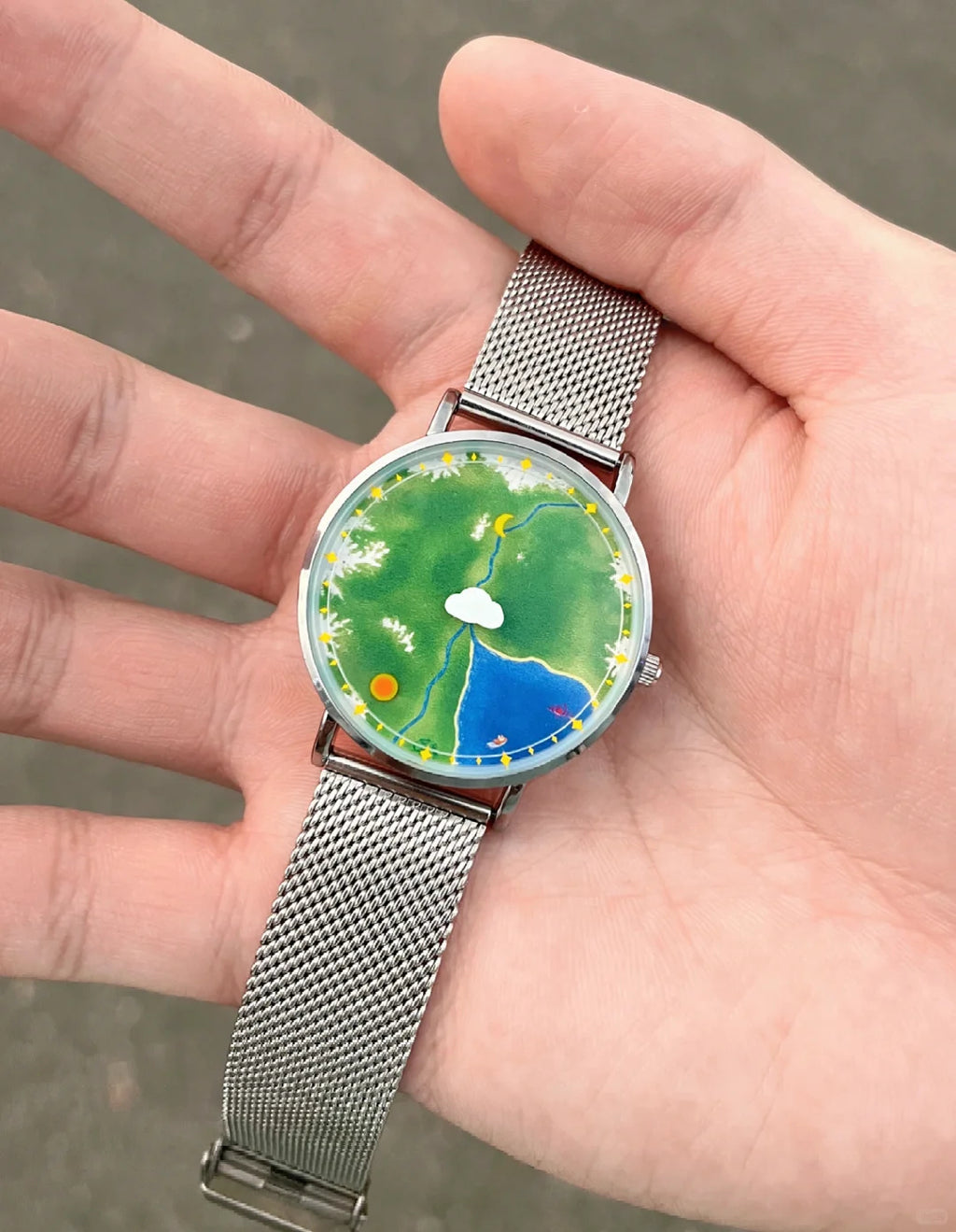 Nature's Orbit Earth landscape watch with silver mesh strap held in hand