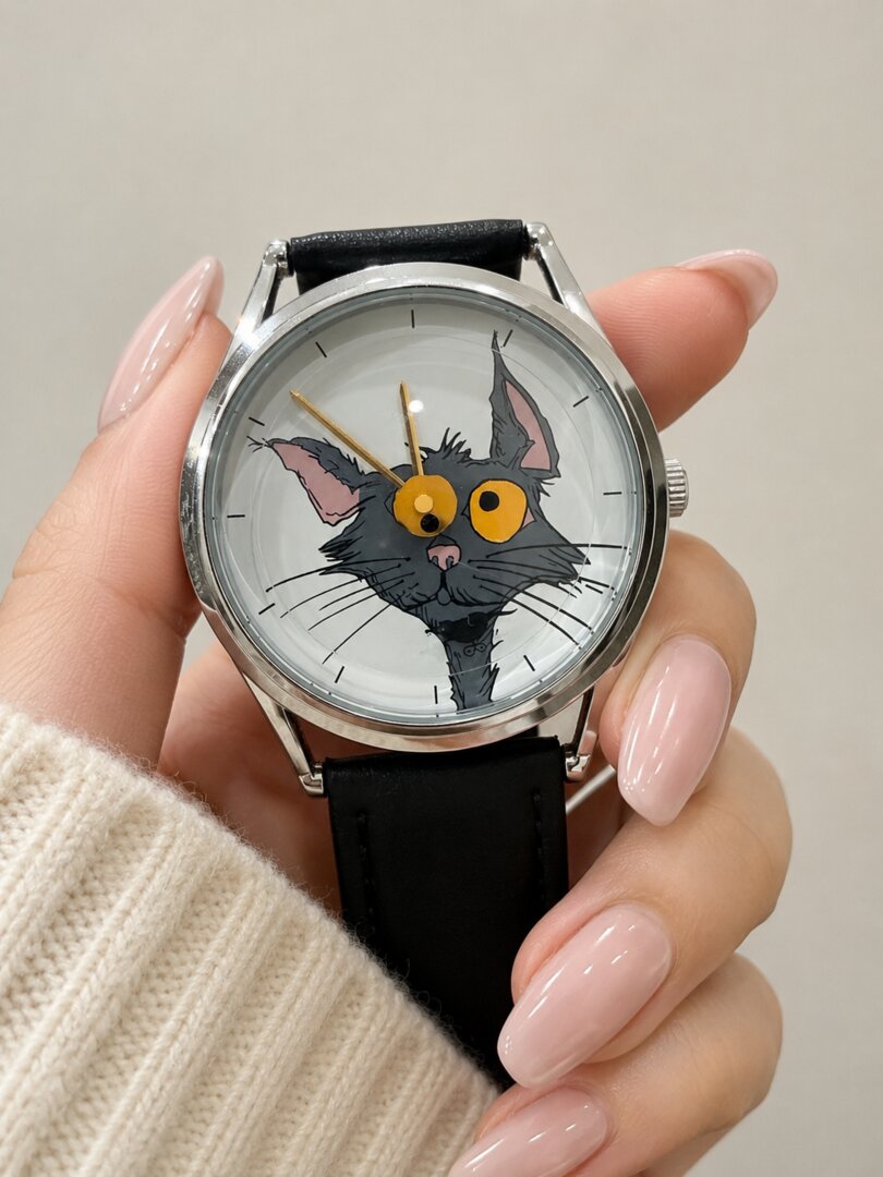 Hand holding Chase Me, Kitty! watch with illustrated gray cat dial, yellow eyes and hands, and black leather strap